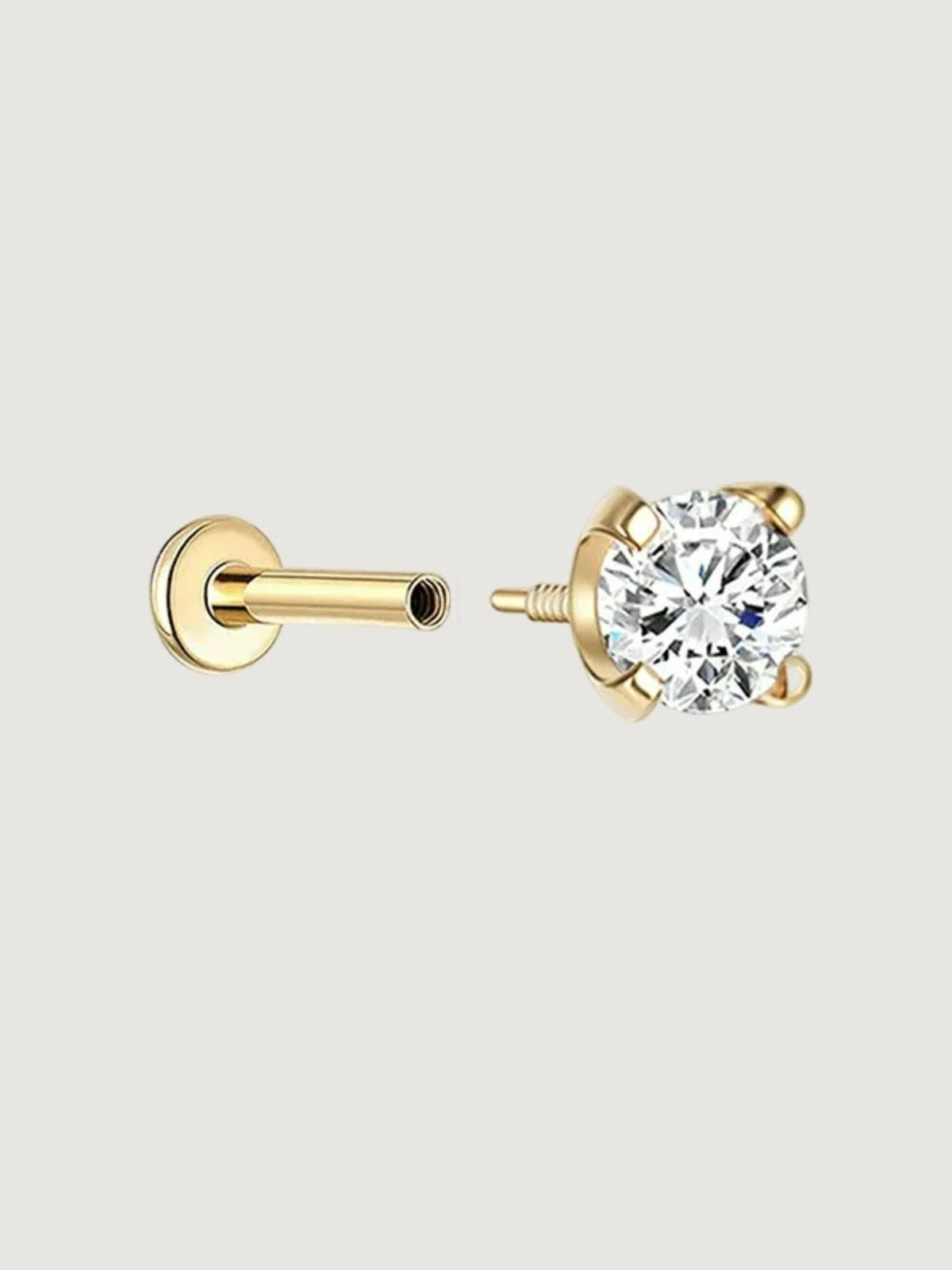 A pair of gold stud earrings shown disassembled on a light gray background, with one earring showing the round clear gemstone in a prong setting and the other showing the post and backing.